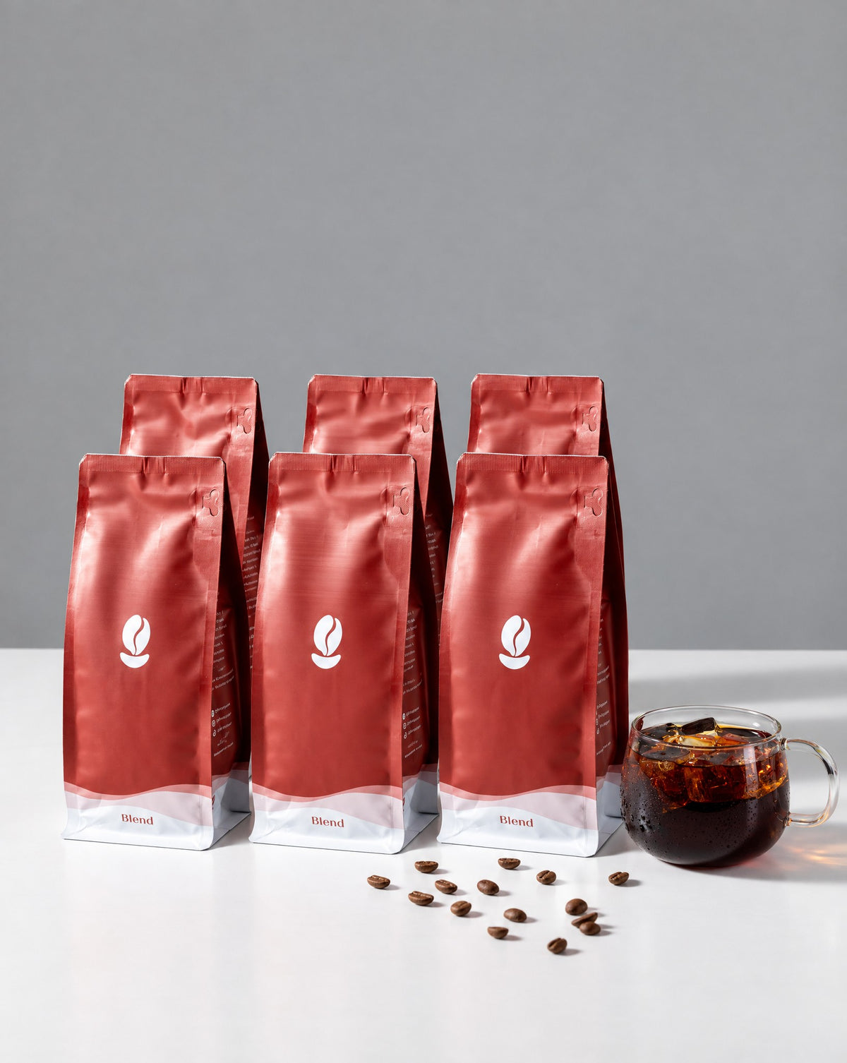 The Full House: six 300g Bean Shipper bags and a glass of iced black coffee on a white table against a grey wall