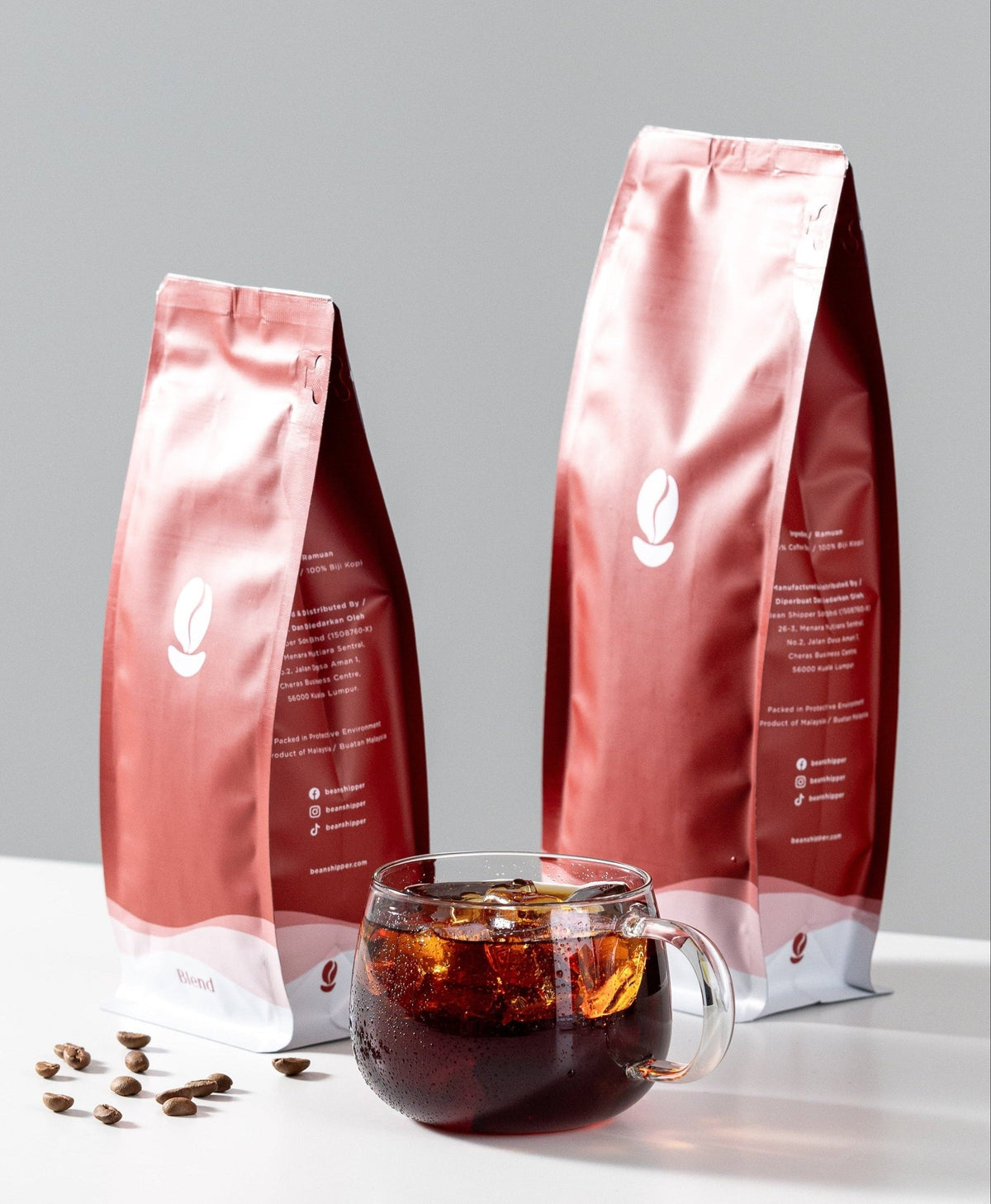 Two red coffee bags with a glass of iced coffee on a white surface.