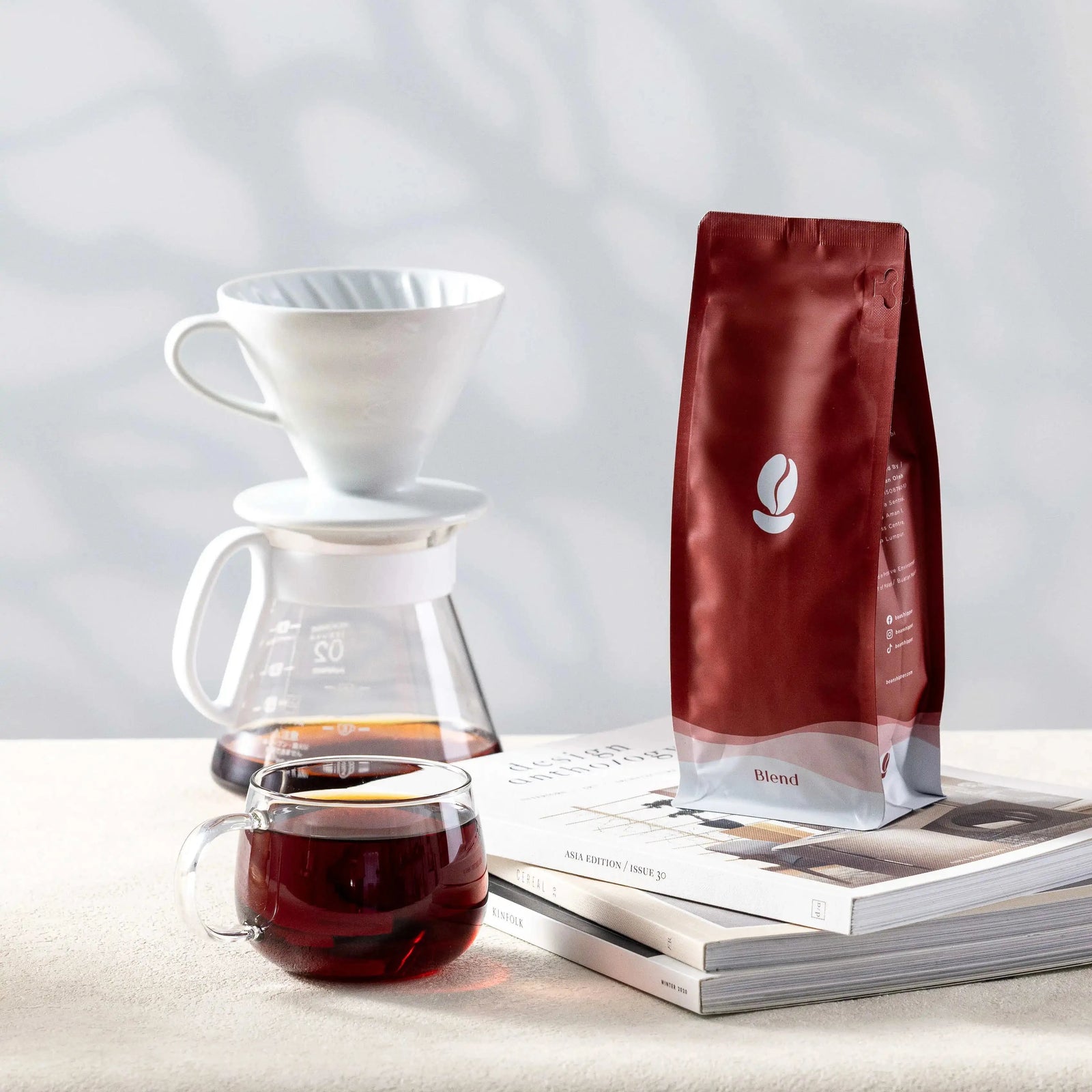 Coffee-making setup with a pour-over coffee maker, coffee bag, and cup of coffee on a light surface.