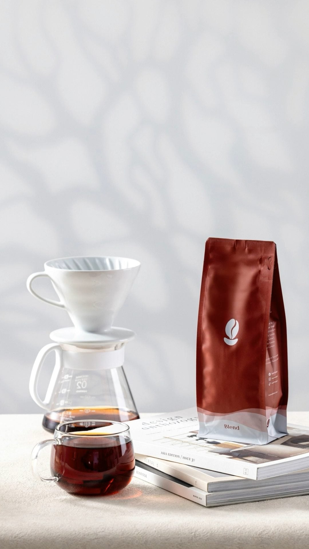 A red Bean Shipper Blend bag beside a pour-over dripper and a glass cup of black coffee