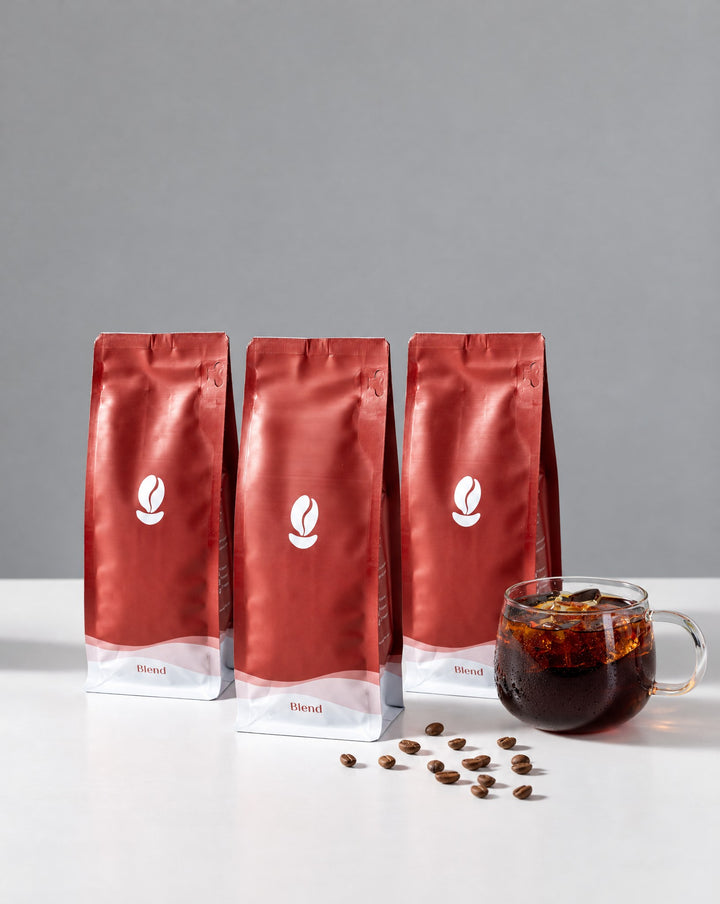 Dessert Trio, Medium Roast: three 300g Bean Shipper bags and a glass of iced black coffee on a white table against a grey wall