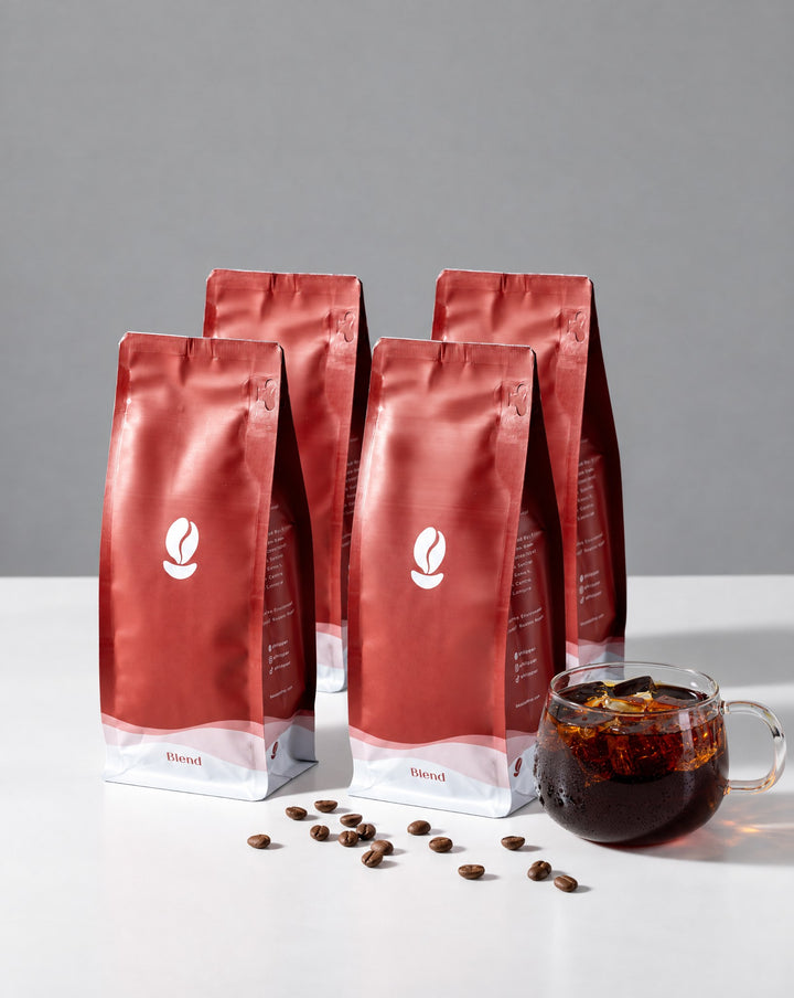 Ritual Pack: four 300g Bean Shipper bags and a glass of iced black coffee on a white table against a grey wall
